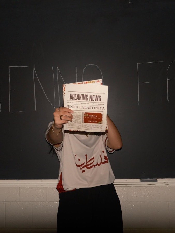 A member in a Palestine football shirt holds up the Henna Falastiniya program, printed as a newspaper front page