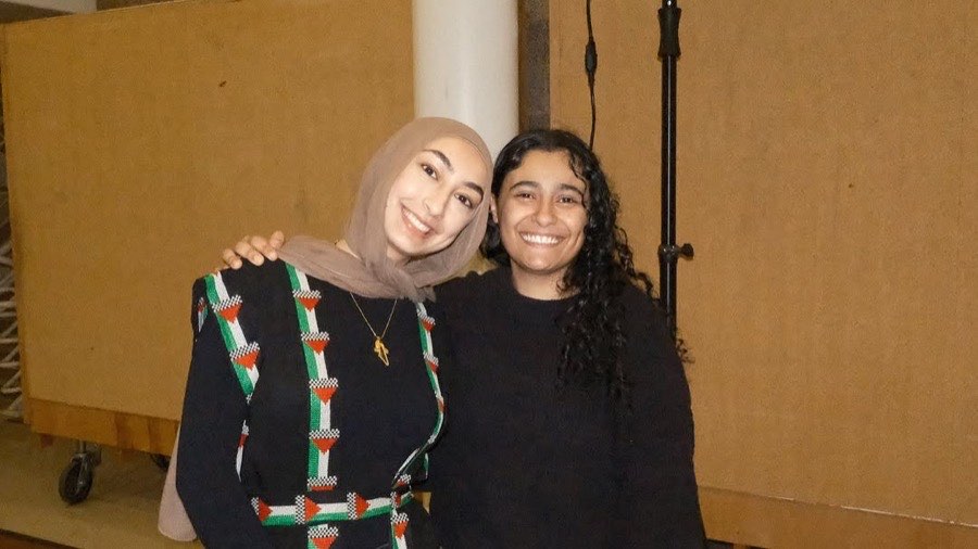 Two members smiling together, one wearing a thobe with tatreez in the colors of the flag